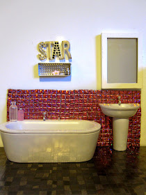 Modern dolls house miniature bathroom with pink sparkly tiles on the wall and grey shiny 'stone' floor.