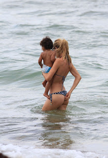Doutzen Kroes adjusting her bikini underwear and holding a child