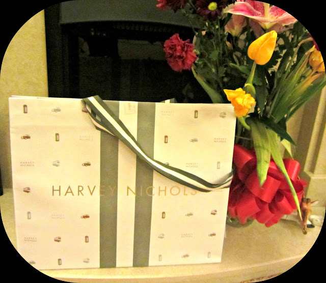 A picture of a Harvey Nichols large bag by a fire place and some flowers