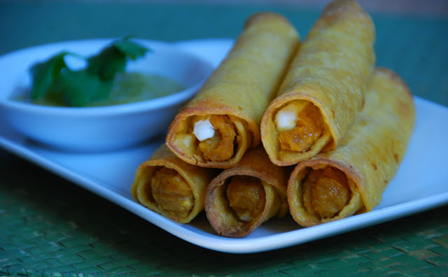 close up of rolled taquitos on white plate with cup of salsa
