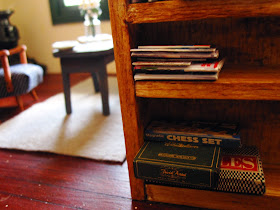Dolls house miniatrie bookcase with a stack of game boxes on the bottom shelf.