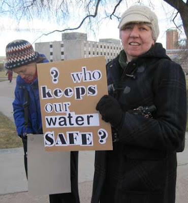 Woman with ransom note-style sign reading Who will keep our water safe?