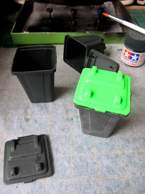 Three modern dolls' house miniature wheelie bins, on a workbench after being painted.