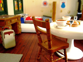 Interior of a miniature holiday home with a suitcase in one corner and a table set with two bowls of soup and glasses of wine, and a loaf of crusty bread in the other.