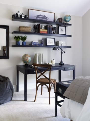 Bedroom with a dark wood desk with matching floating shelves, a mirror, bean bag chair and trunk at the foot of the bed