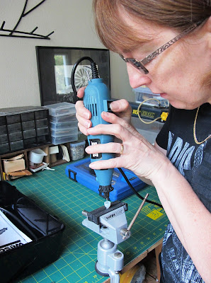 Woman drilling a hole in a modern miniature lamp shade being held in a vice.