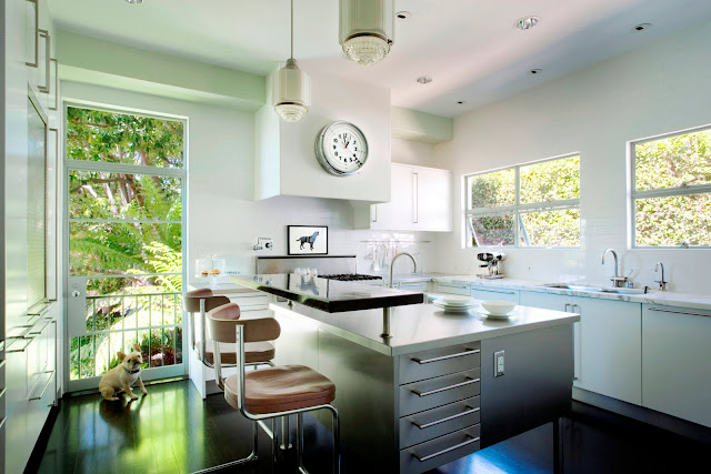 Kitchen from Kitchens and Baths by Michael S. Smith with stainless island with long drawer pulls, a black floor, white cabinets, two pendant lights and stainless appliances