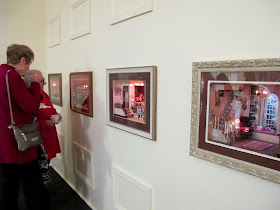 Customers admiring dolls' house miniature room boxes set into the wall.