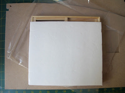 Pieces of a dollshouse building kit with a sliding door unit on top, covered with a piece of card, showing space at the top.