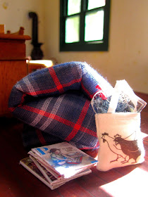 Inside of a miniature holiday house, showing a doona rolled up on the floor next to a pile of magazines and a bag of knitting.