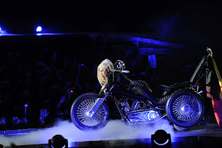 Lady Gagawearing a leather outfit and laying on a morotcycle