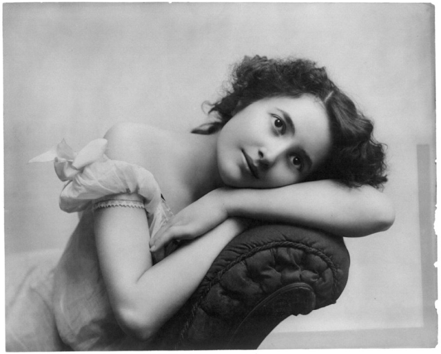 antique photo of young woman laying on a sofa in cotton gauzy nightgown with bows on arms