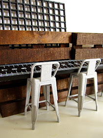 Modern dolls' house miniature cafe stools in front of a counter made from a ruler and miniature pallets.