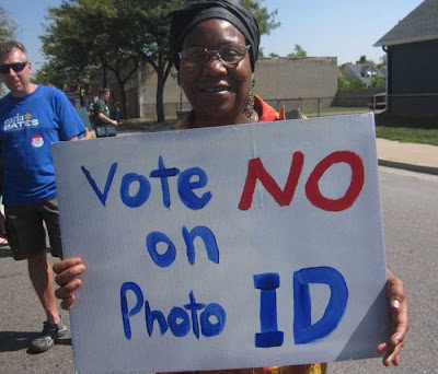 Woman holding hand-painted sign reading Vote No on Voter ID