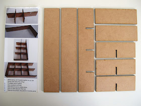 Components of a  modern dolls' house miniature laser-cut 'pidgeon' hole kit laid out on a work table.