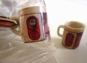 Two modern dolls' house miniature mugs with a design of a Canberra bus shelter. On the left is the (clearer) photo version, clamped to dry. On the right is the (less clear) decal version.