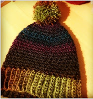 A beanie made in February 2014, made of Bouvardia yarn in "Shadow Spectrum" colours. The pom pom and ribbing are light green and the body is in dark purple and turquoise colours.