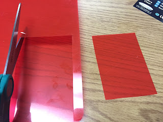 Scissors cutting a red plastic folder into small rectangles.