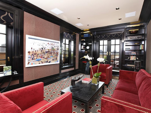 Black lacquer den with red velvet sofa chairs with nailhead trim, red and black graphic rug, black french doors and encasement windows, black and gold Roman shades, and a black built in book case
