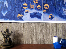Modern dolls' house miniature scene showing a blue and gold modern chinese panel on the wall. Underneath is a sideboard with a variety of blue and gold items on it.