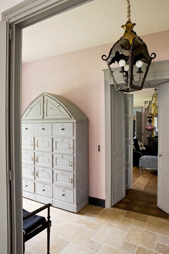 Pink and grey foyer in a French mansion with stone tile floor, lantern light, double doors leading to the living room and an arched cabinet