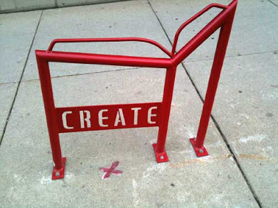 Red metal bike rack shaped like an open book with the word CREATE in open stencil letters