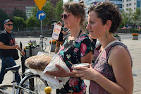 Dwie osoby, trzymające w wyciągniętych dłoniach bochen chleba oraz miskę z solą. Zdjęcie z demonstracji "Witamy uchodźców Chlebem i Solą" z 25 lipca w Warszawie