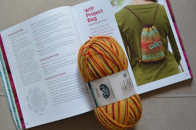 The book "Crocheted One-skein Wonders" is open to the page of the pattern which displays a photograph of the finished item. A skein of multicoloured sock yarn is resting on top, holding the book open.