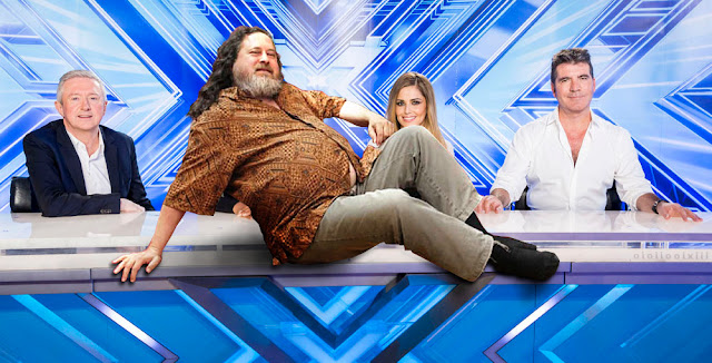 Richard Stallman lies, gallant, atop the xFactor desk, with the judges seated behind.