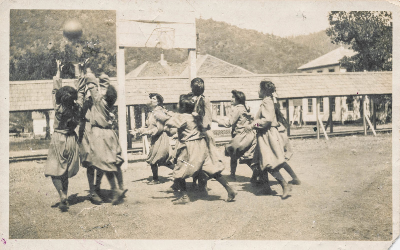 School girls in athletic bloomers playing basketball outdoors, ca. late