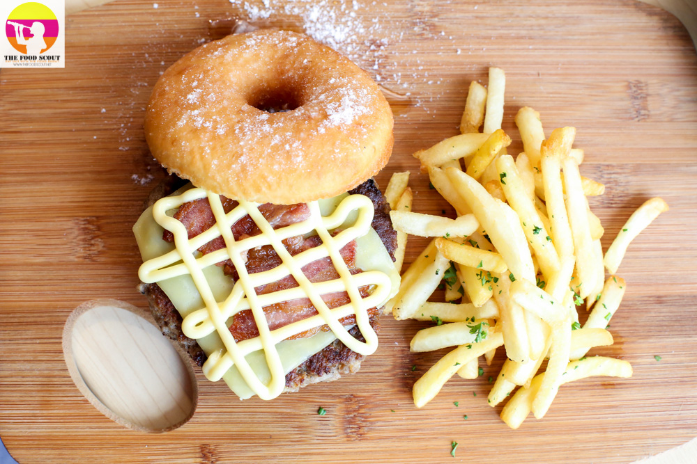 A table serving a donut hamburger with cheese on top and fries beside