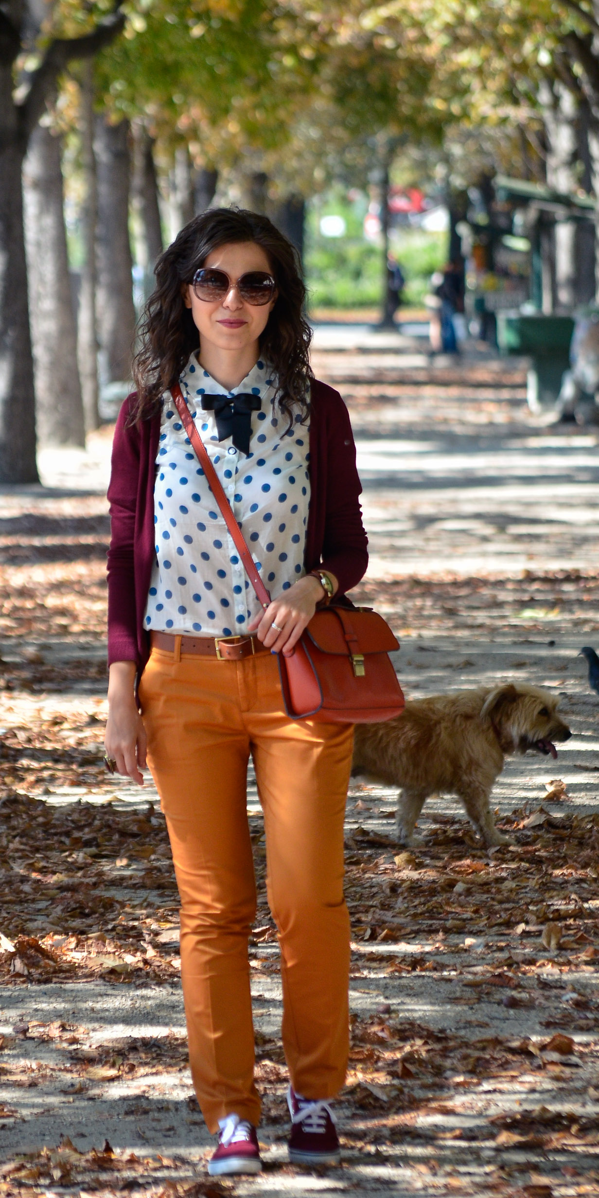 preppy fall outfit in Paris mustard pants burgundy sweater sneakers H&M orange satchel bag dotted shirt blue dots black bow tie champs elysees jardin de tuileries eiffel tower