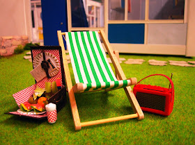 Miniature deck chair, radio and filled picnic hamper on the lawns in front of a miniature Rose Seidler house.