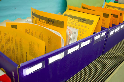 Blue mailboxes filled with student papers and newsletters resting on classroom radiator.