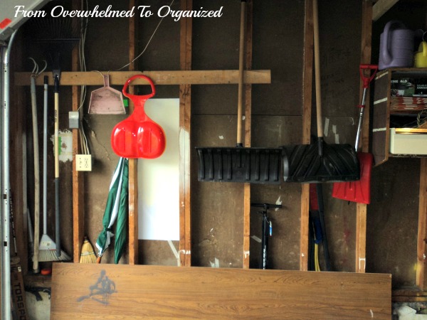 Wall of garage with hanging shovels and brooms.