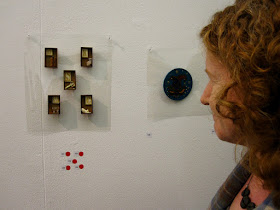 A woman admiring five sold brooches on display in a gallery.