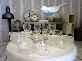 Close up of  a modern dolls' house miniature display of glass bowls, plates and glasses, set out on a round white table in a homeware store.
