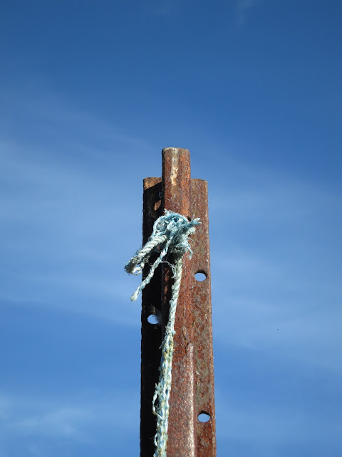 Frayed blue nylon rope tied through hole on rusty pole in front of deep blue sky