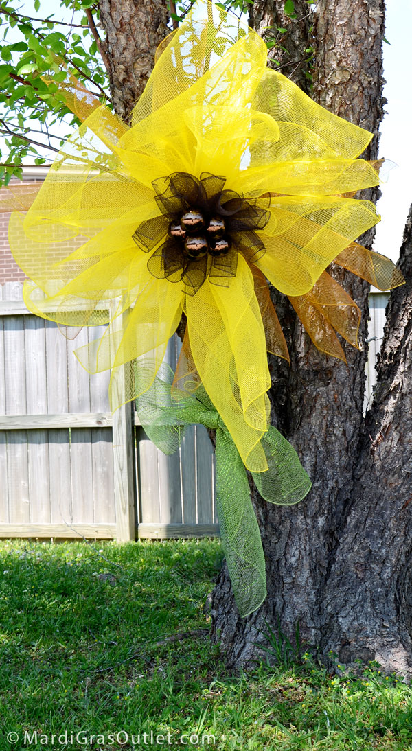 Festive deco mesh sunflower displayed outside on a tree.