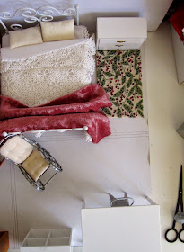 View from above of shabby chic dolls' house miniature furniture bedroom setting arranged on a piece of cardboard.