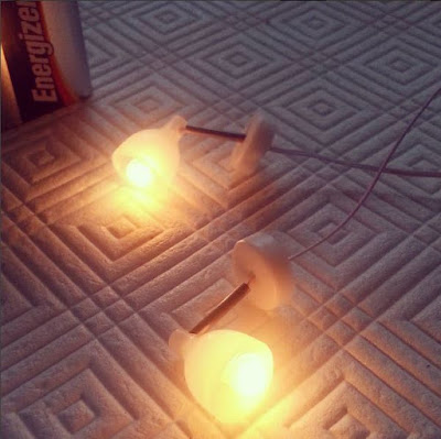 Two modern miniature wall lamps, light by a 9-volt battery, on a table.