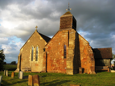 New church butting against old church illuminated by evening sunlight and stormy skies