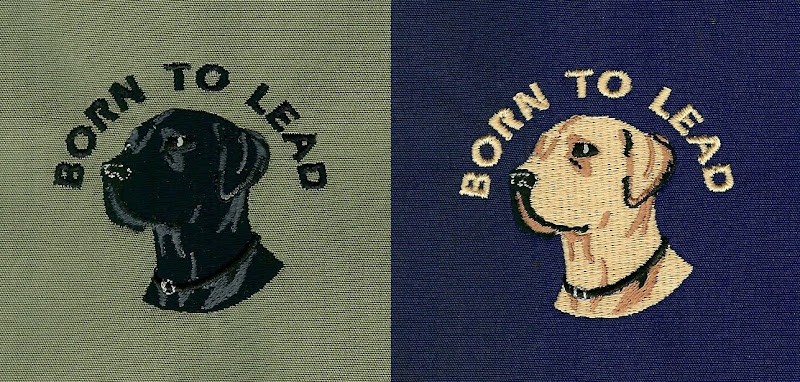 embroidered black lab on clover green background, yellow lab embroidered on navy background, both have born to lead in an arch over the dog