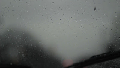Rain drops fall on a car windshield while the wipers push them away
