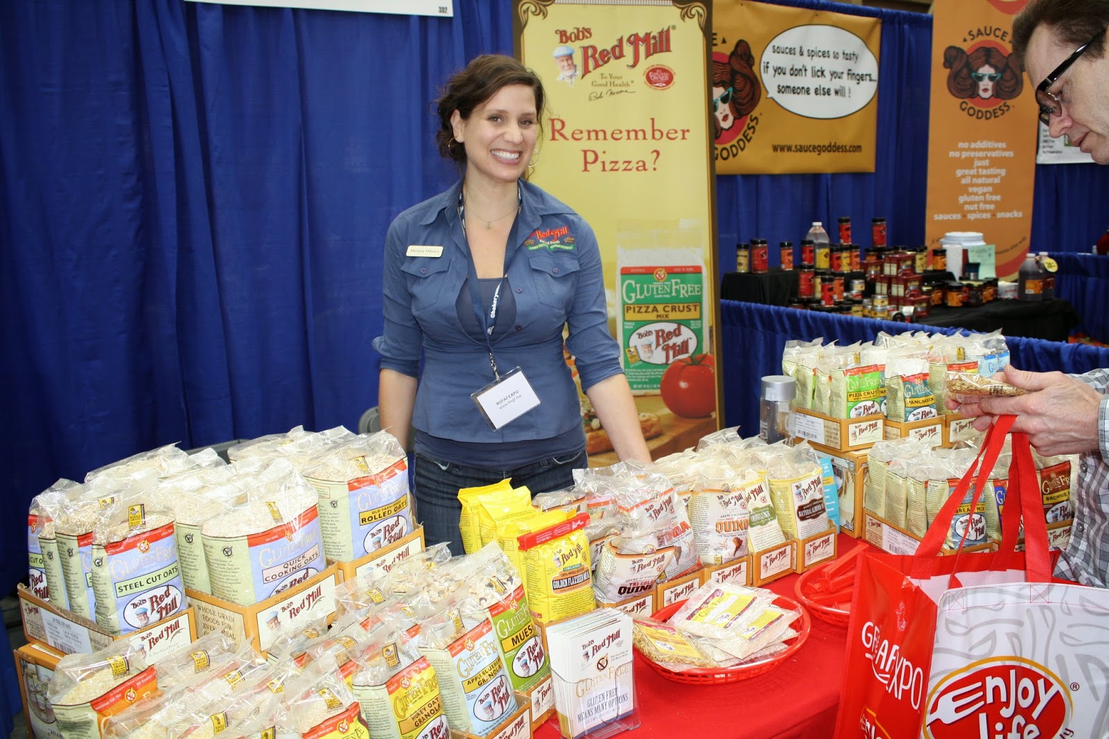 Bob's Red Mill booth with smiling rep and a table full of bagged flours and products