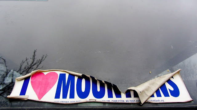 An 'I Love Mountains' bumper sticker on the back window of a car in Denver.