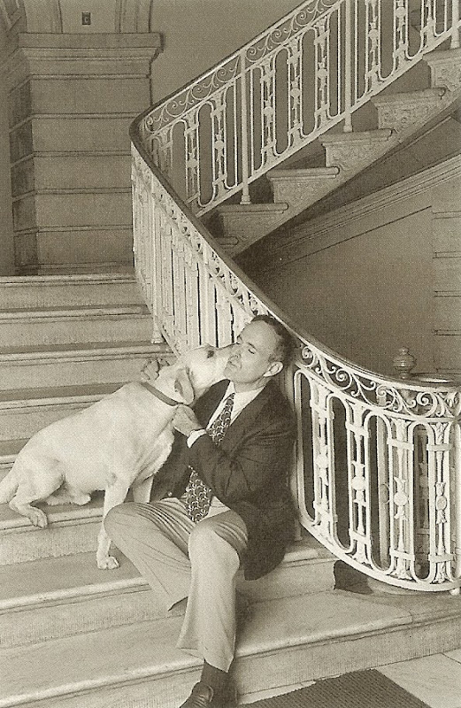 black and white photo of a young Rudy Giuliani sitting on a staircase, getting kissed on the cheek by a yellow lab
