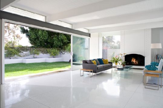 Living room with a large glass sliding door, white tile floor, fireplace, and a grey sofa with blue and green accent pillows