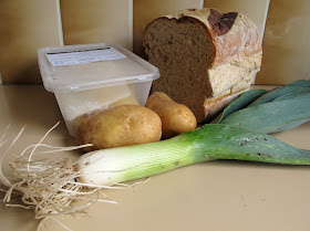 A container of fresh pasta, half a loaf of bread, two potatoes and a leek arranged on a kitchen bench.
