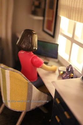 Modern dolls' house miniature study with a doll working on a Mac computer.